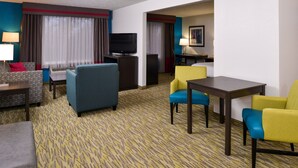 Une chambre d’hôtel équipée d’un canapé, de fauteuils, d’une télévision, d’un bureau et d’une table à manger.