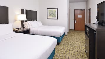 A hotel room with two beds, a desk with a lamp, a television, and a door.