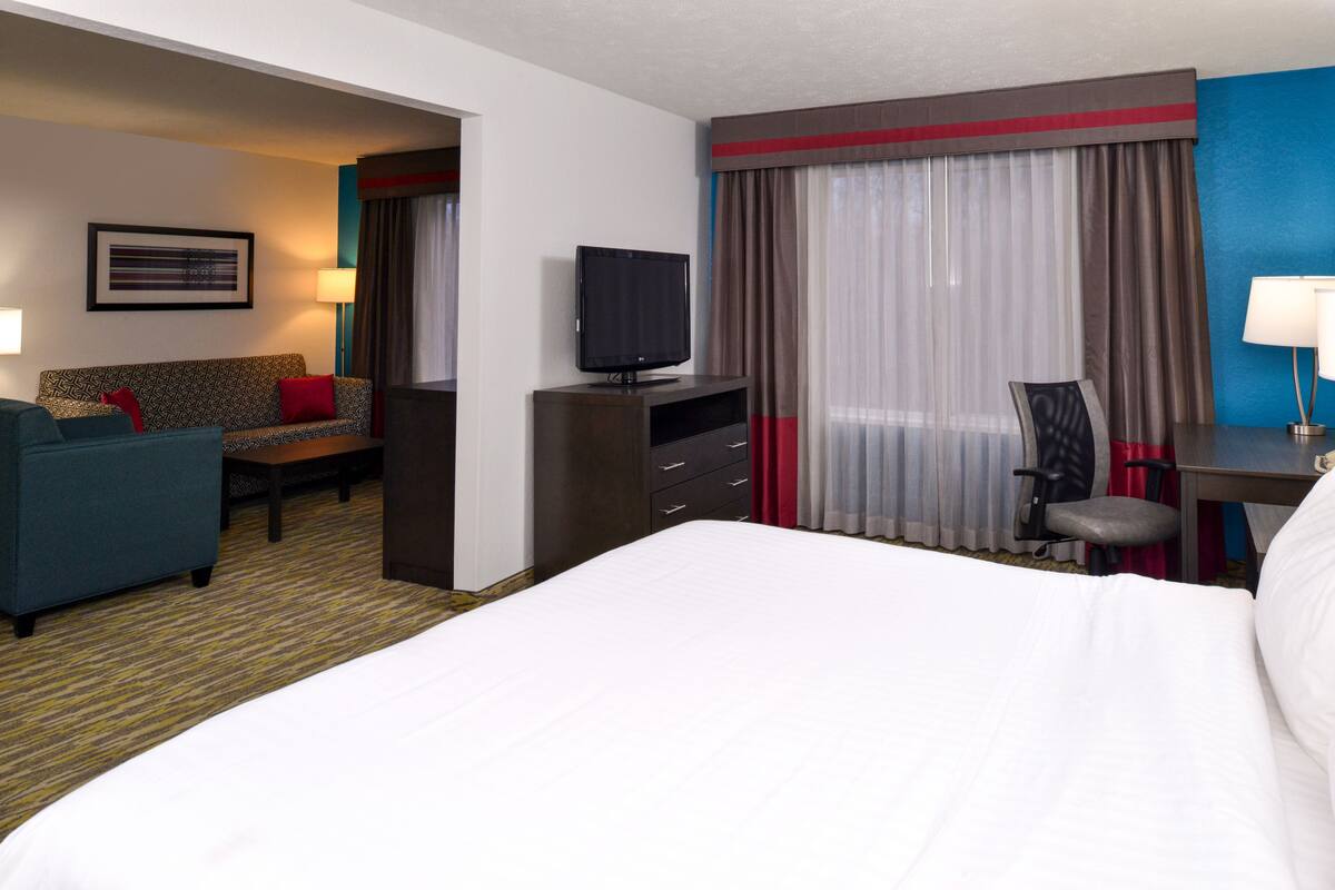 A hotel room with a bed, a TV, a desk, a chair, a sofa, and a desk lamp.
