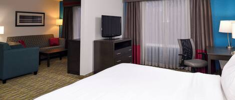 Habitación de hotel con cama, escritorio, silla, televisor, sofá y lámpara de escritorio.