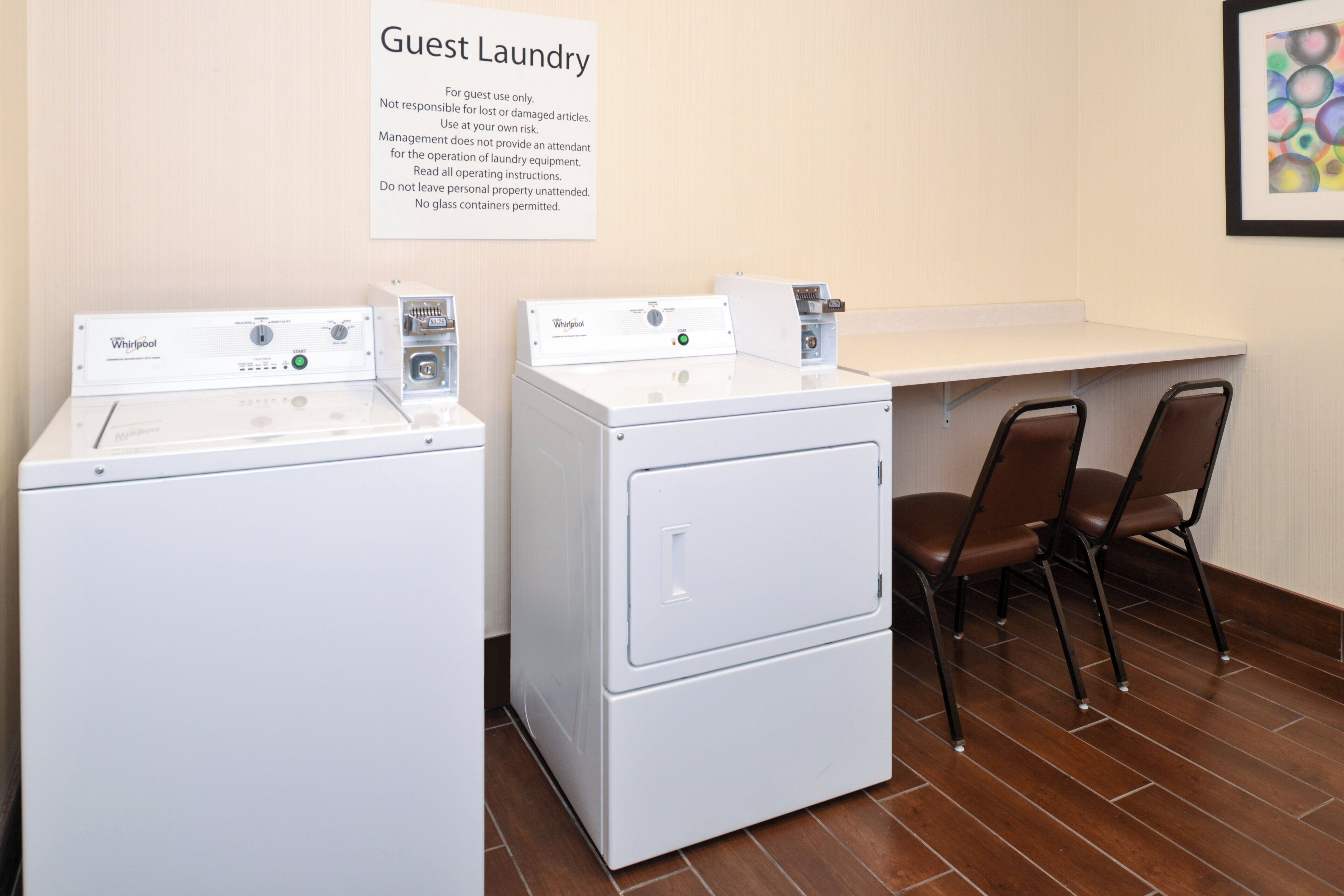 A guest laundry area with Whirlpool washers and dryers, a sign with operating instructions, and a seating area with chairs.