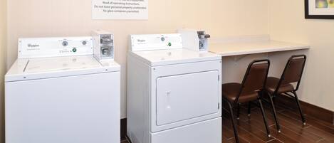A guest laundry area with Whirlpool washers and dryers, a sign with operating instructions, and a seating area with chairs.