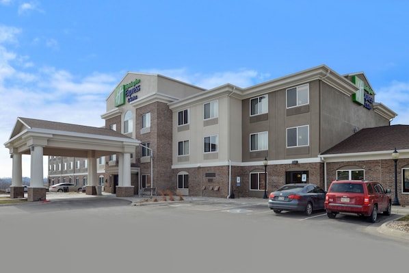 A hotel with a covered entrance, multiple floors, and a parking area with cars.