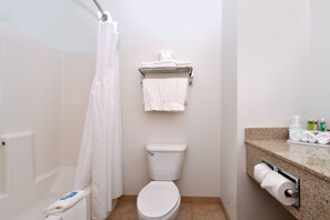 Une petite salle de bain propre, équipée de toilettes, d’un rideau de douche, d’un porte-serviettes et d’un support à papier toilette.