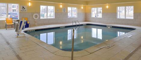 An indoor swimming pool with clear water, tiled walls, and windows.