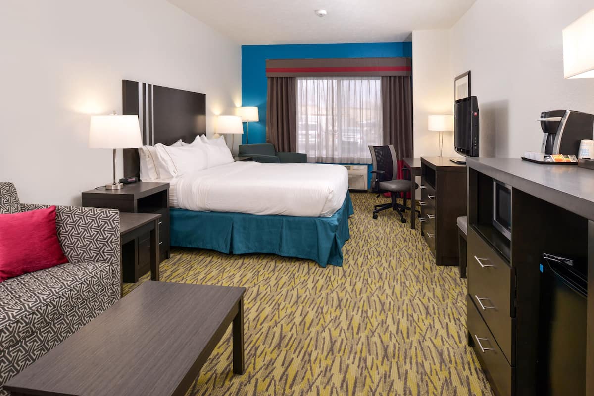 A hotel room with a bed, a desk, a chair, a TV, and a coffee machine.