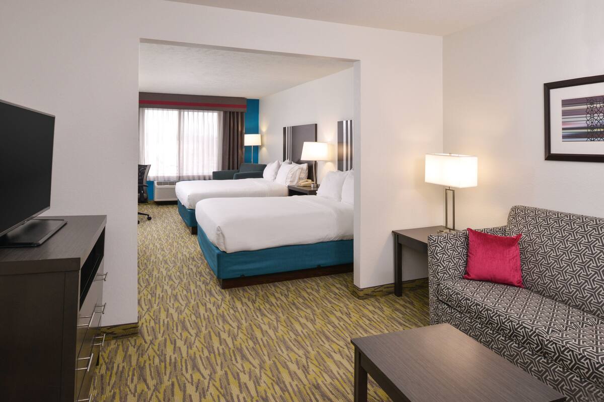 A hotel room with two beds, a sofa, a TV, a desk, and a lamp.