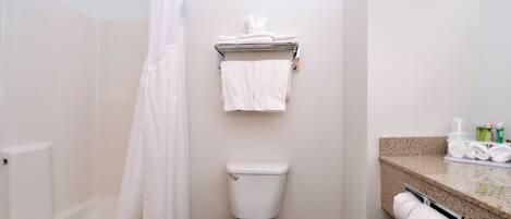 A bathroom with a toilet, a shower curtain, a towel rack with towels, and a countertop with toiletries.