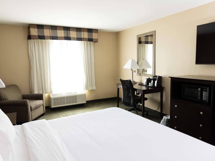 A hotel room with a large bed, a desk with a chair, a television, a mirror, and a window with curtains.