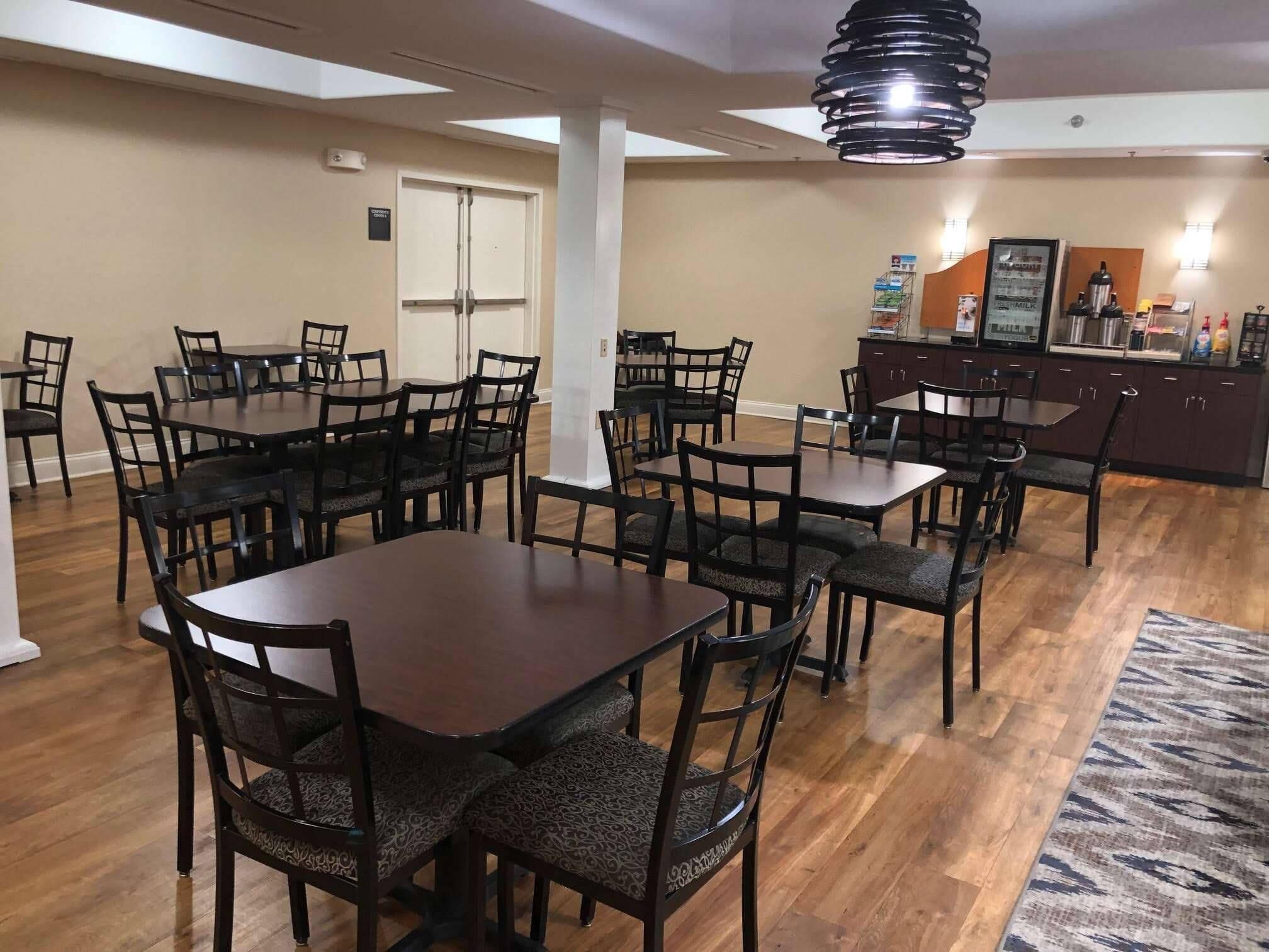 A dining area with multiple tables and chairs, a kitchen area with a refrigerator and cabinets, and a patterned rug on the floor.