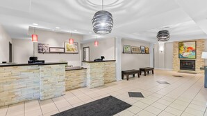 A reception area with a stone counter, two pendant lights, framed artwork on the walls, and a fireplace in the background. - Country Inn & Suites by Radisson, Elizabethtown, KY (Elizabethtown)