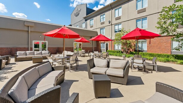 An outdoor patio area with wicker furniture, red umbrellas, and a brick building in the background. - Country Inn & Suites by Radisson, Elizabethtown, KY (Elizabethtown)
