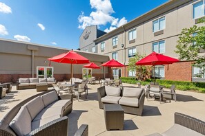 An outdoor patio area with wicker furniture, red umbrellas, and a brick building in the background. - Country Inn & Suites by Radisson, Elizabethtown, KY (Elizabethtown)