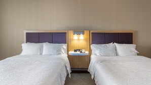 Una habitación de hotel con dos camas, una mesita de noche pequeña y una lámpara fijada en la pared.