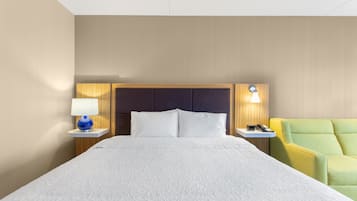 Una habitación de hotel con una cama grande, dos mesitas de noche, una lámpara, un teléfono y un sillón verde.