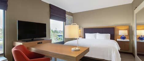 A hotel room with a bed, a desk with a chair, a television, and a window with curtains.