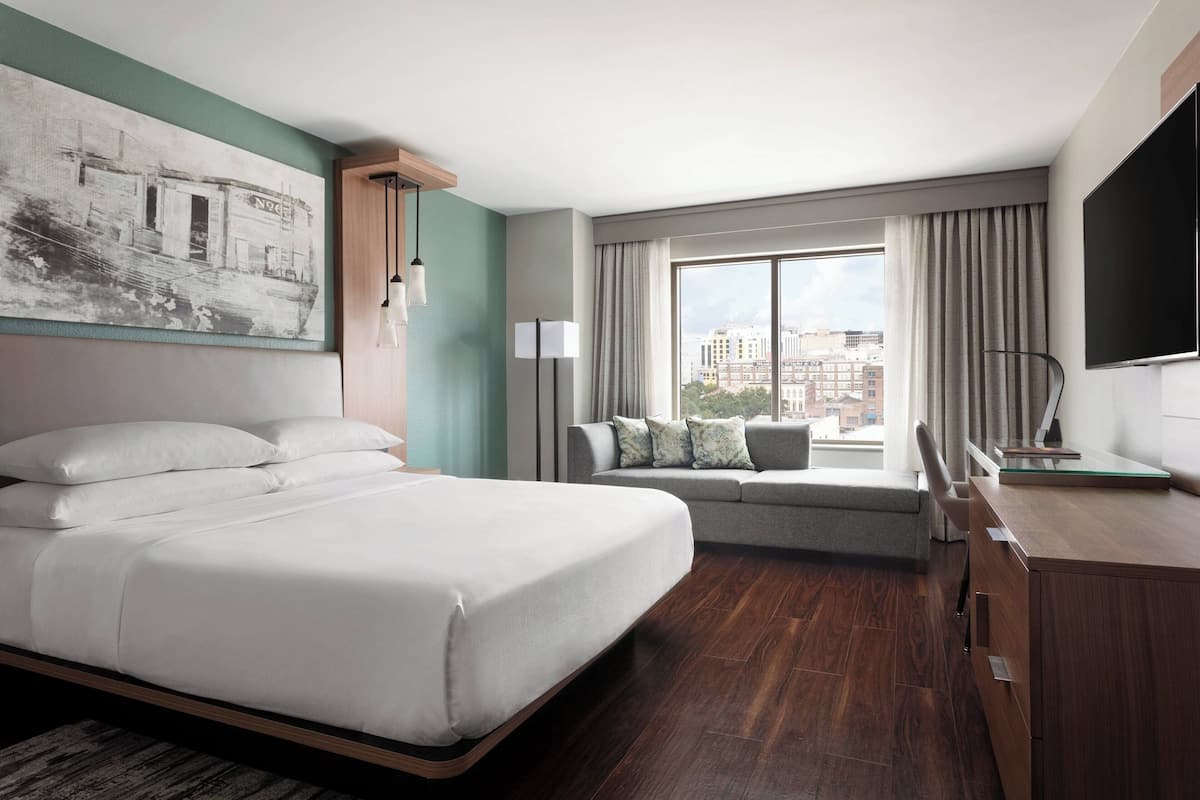 A modern hotel room with a large bed, a sofa, a desk, and a TV.