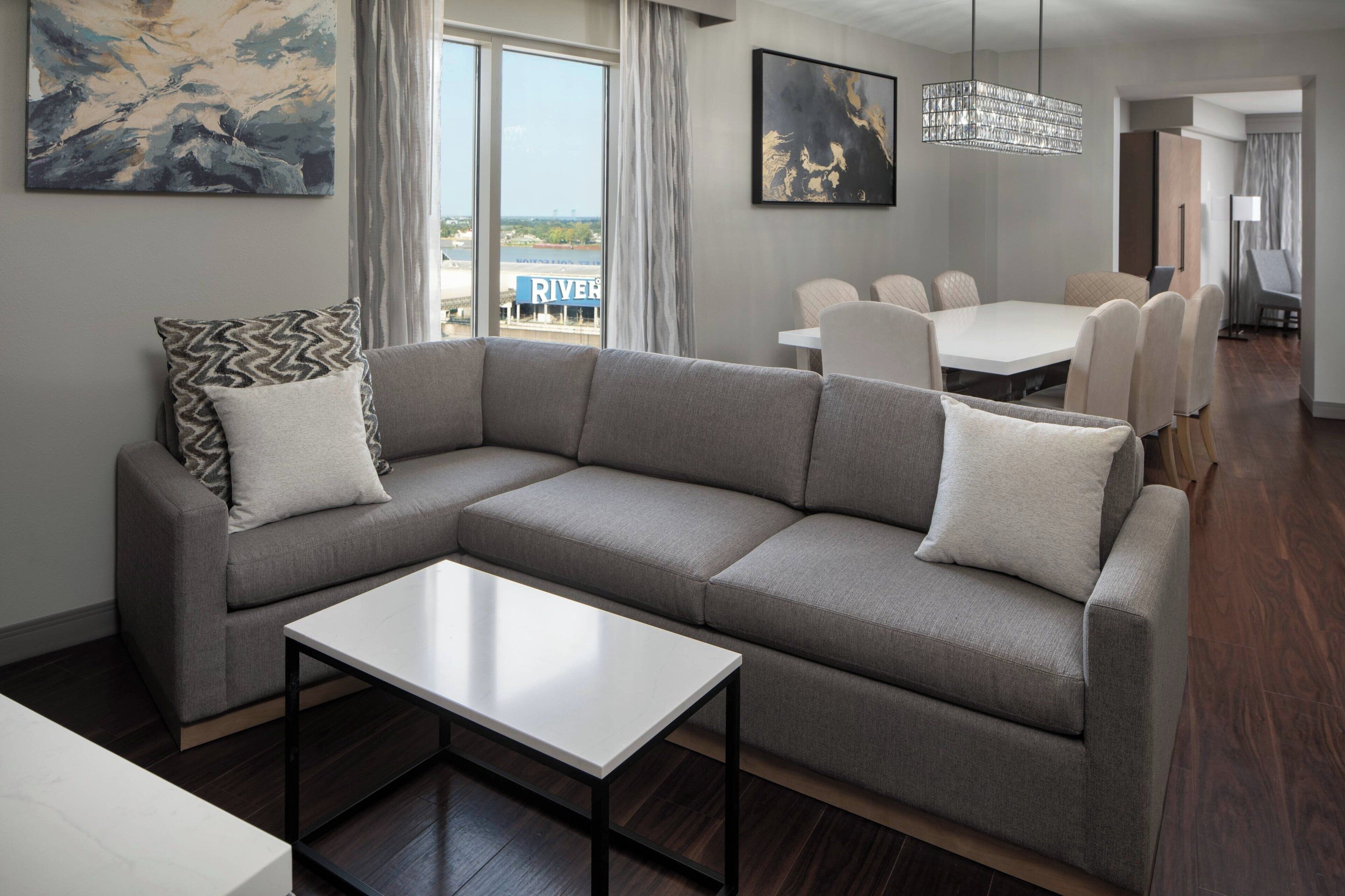 Ein modernes Wohnzimmer mit einem grauen Ecksofa, einem weißen Couchtisch und einem Essbereich mit weißem Tisch und Stühlen.