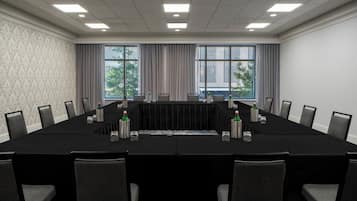 A conference room with a long table, chairs, and windows with curtains.