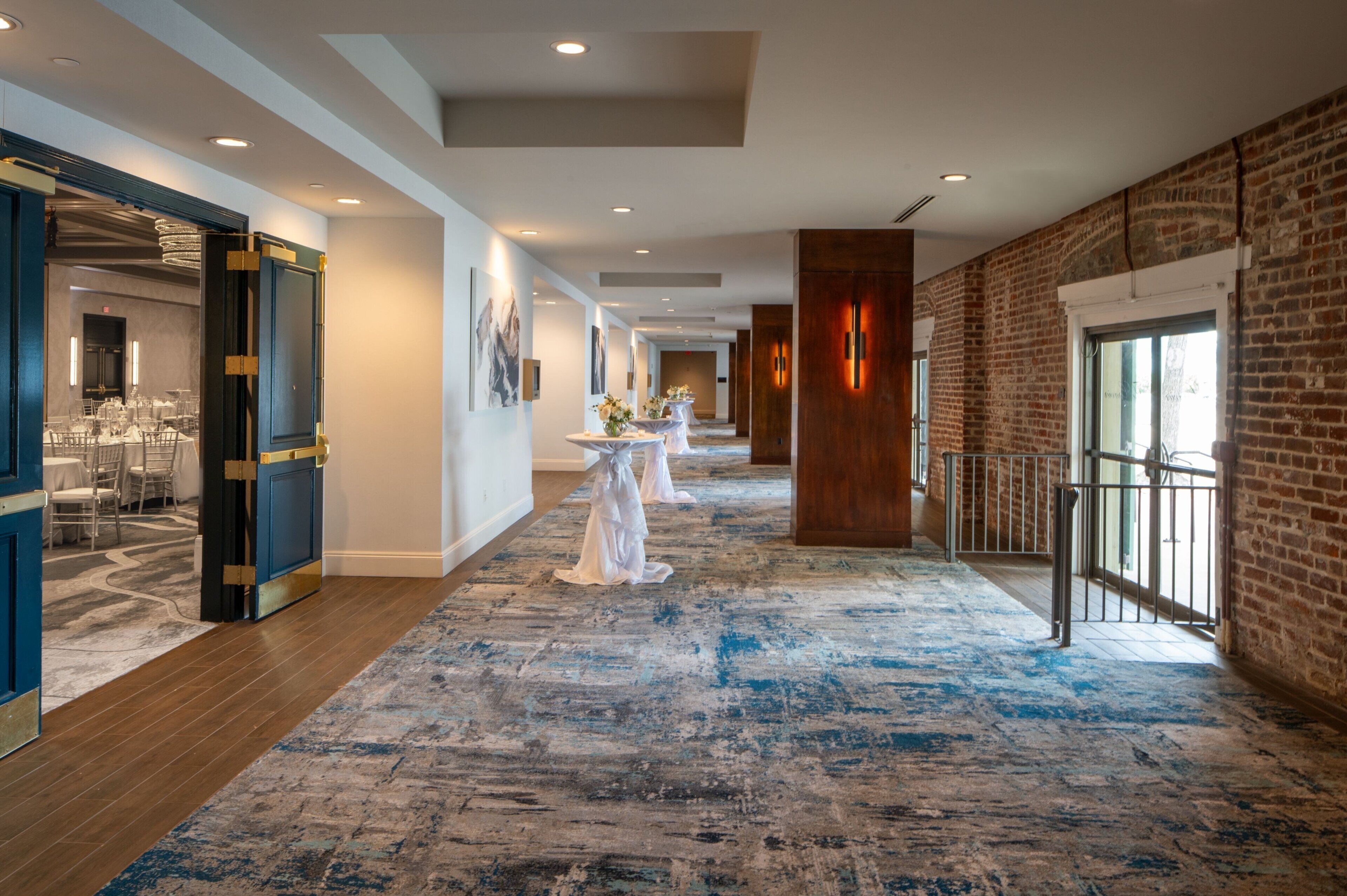 A hotel corridor with a blue carpet, wooden flooring, and brick walls.