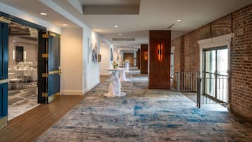 A hotel corridor with a blue carpet, wooden flooring, and brick walls.