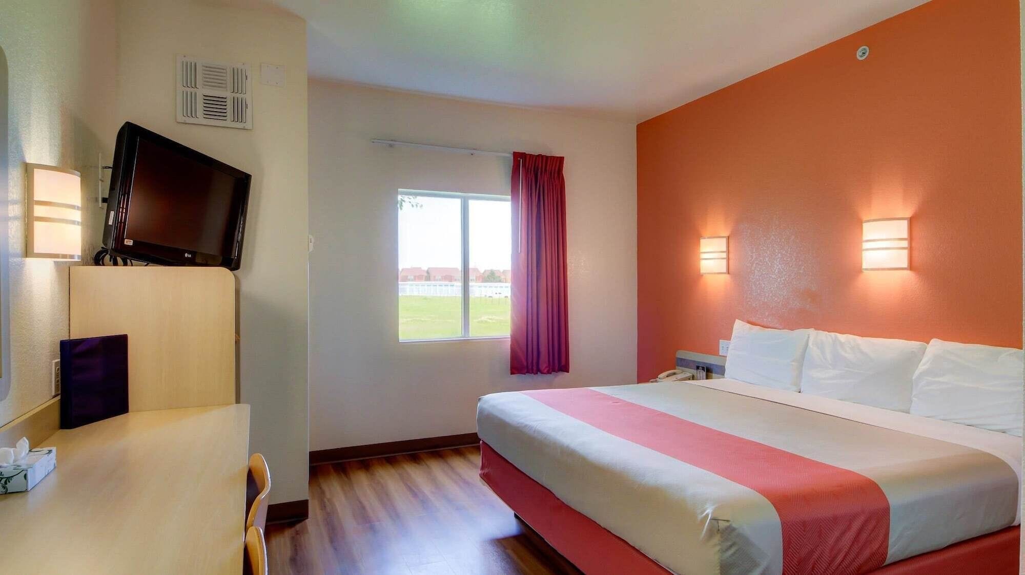 Une chambre d’hôtel dotée d’un grand lit, d’un téléviseur à écran plat fixé au mur, d’un bureau avec une chaise, d’une fenêtre avec des rideaux et de lampes murales.