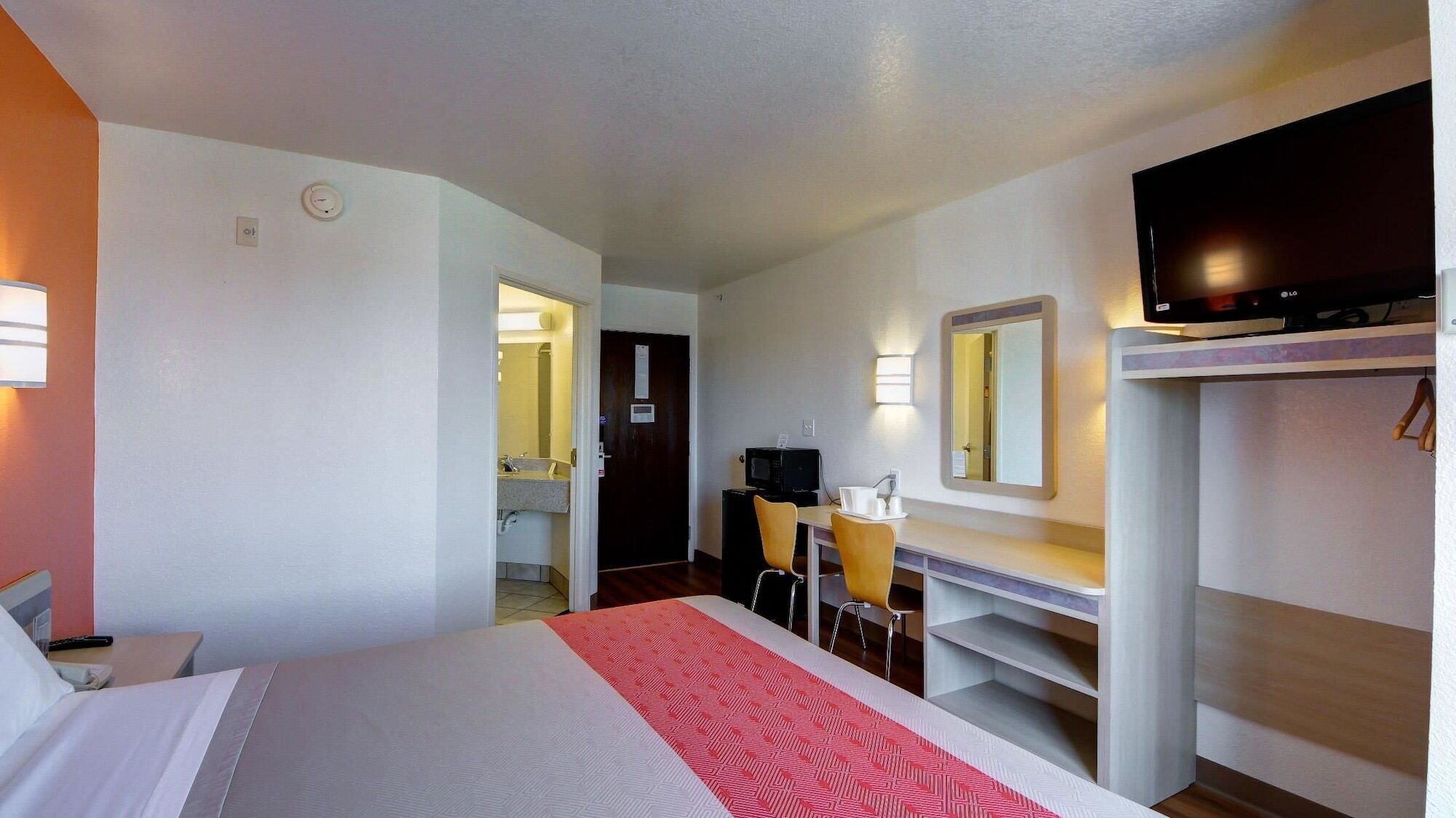 A hotel room with a bed, a desk with a chair, a television, and a mirror.