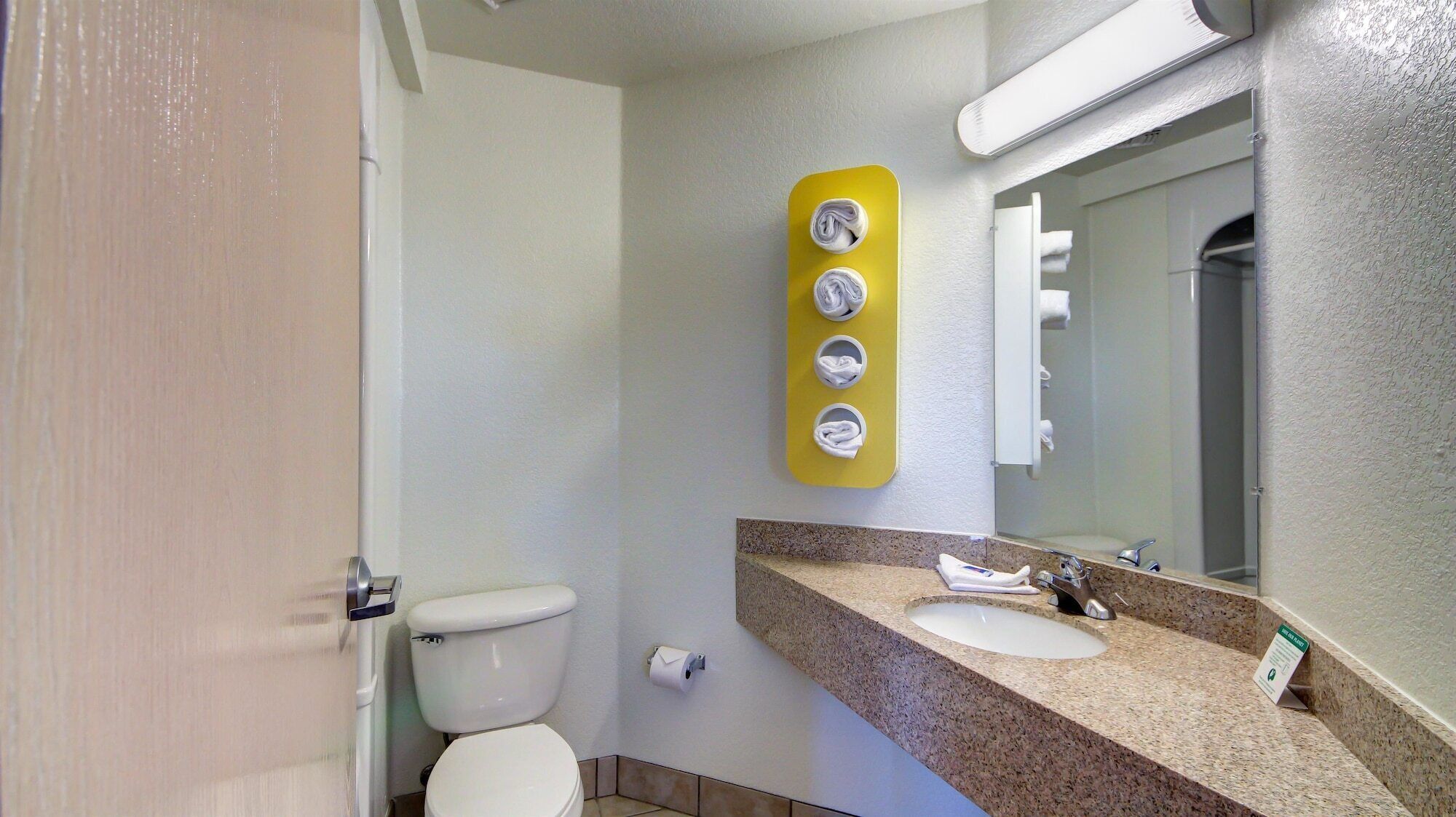A bathroom with a toilet, sink, and a mirror. There is a towel rack with four towels.