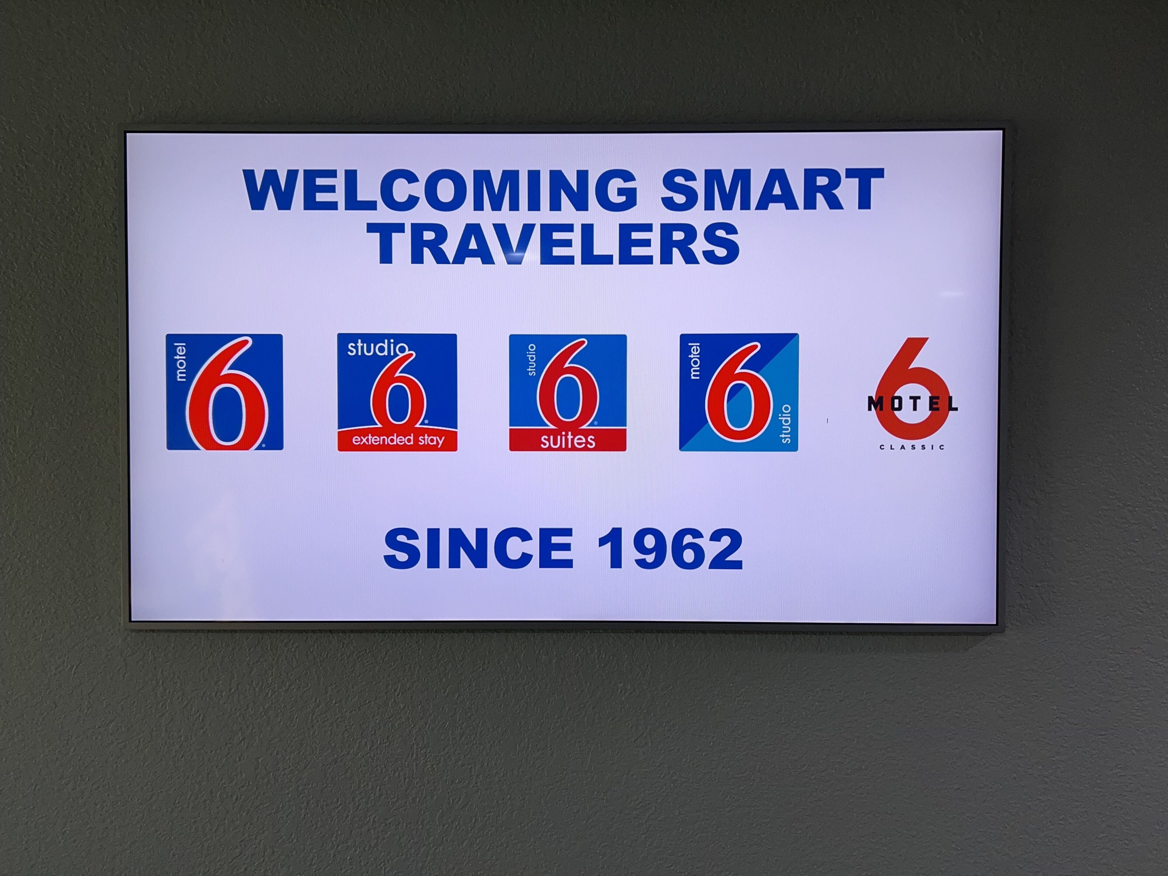 A sign welcoming smart travelers with the Motel 6 logo and different room types since 1962.