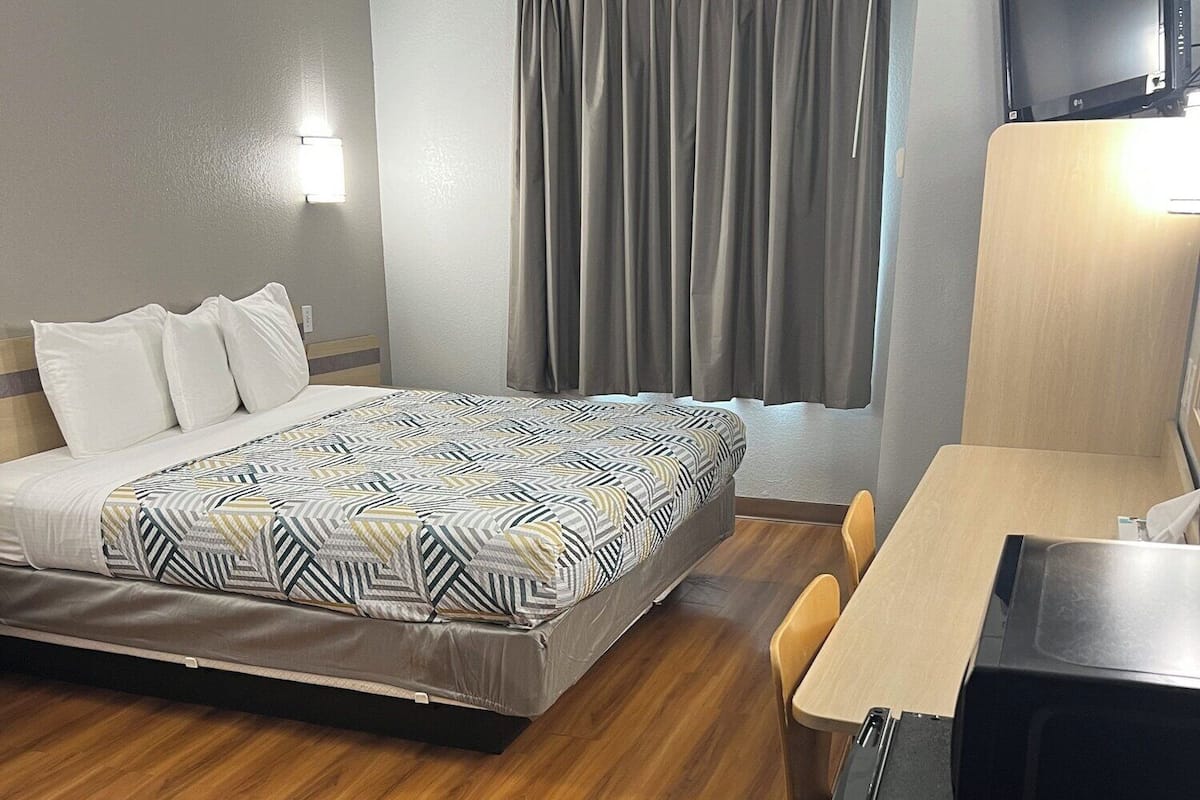 A hotel room with a bed, a desk, a chair, a TV, and a window with curtains.