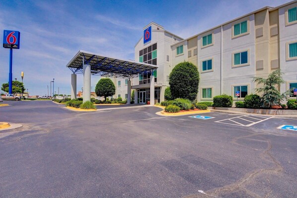 A motel with a covered entrance, multiple parking spaces, and a clear sky.