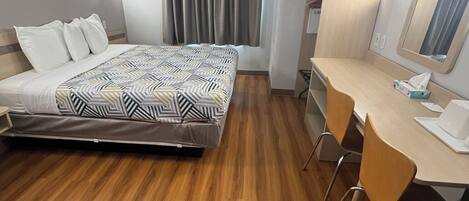 Una habitación de hotel con cama, escritorio con silla, televisor y ventana con cortinas.