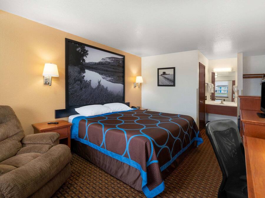 A hotel room with a bed, a chair, a desk with a computer, a TV, and a bathroom.
