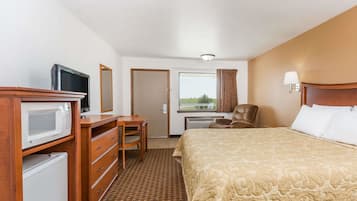 A hotel room with a bed, a desk with a television, a microwave, a chair, and a window with curtains.