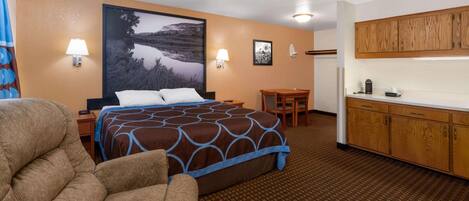 A hotel room with a large bed, a desk, a chair, and a kitchenette.