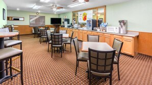 A hotel dining area with tables and chairs, a kitchen counter with appliances, and ceiling fans. - Super 8 by Wyndham Goodland (Goodland)