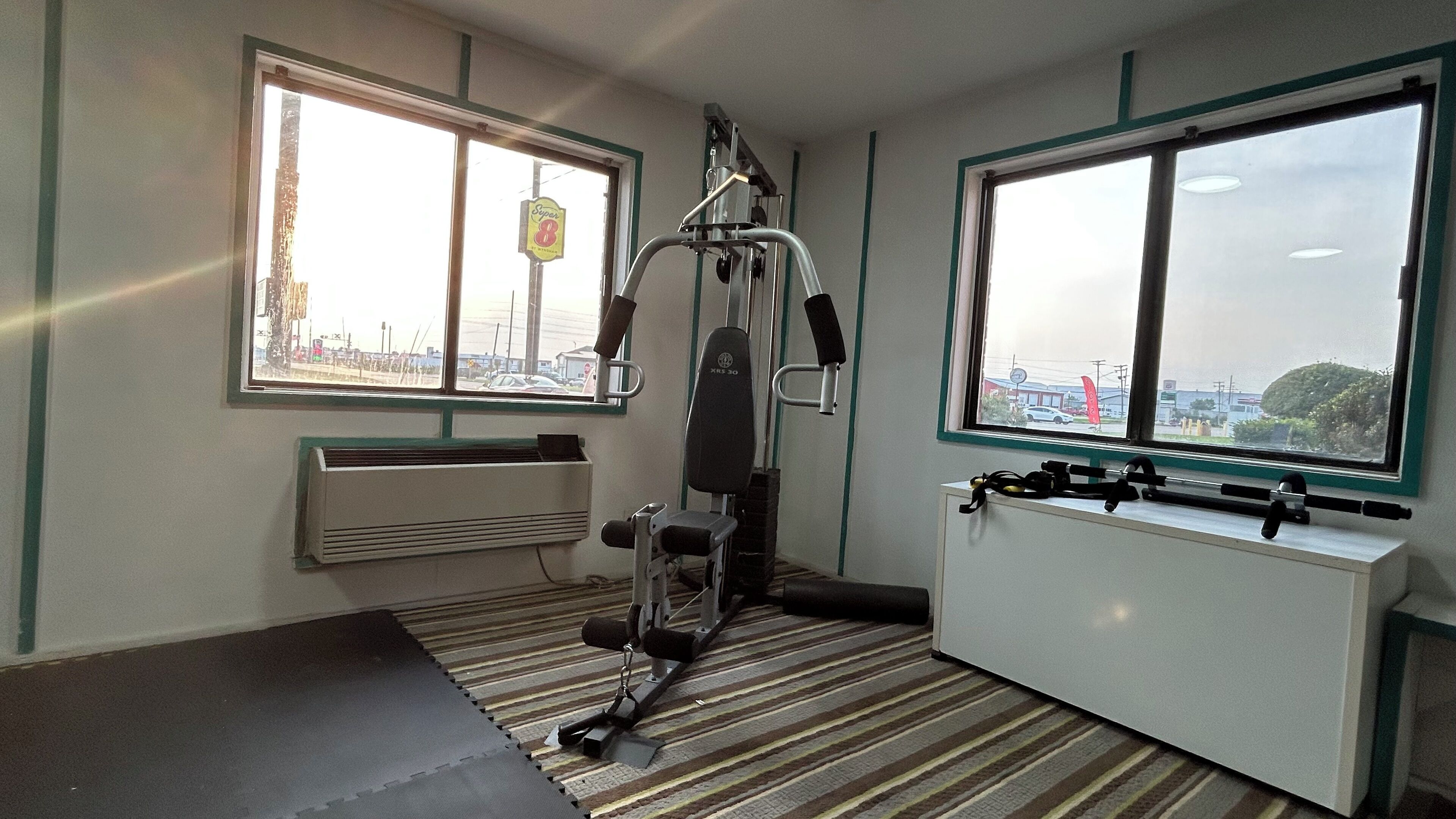 Un gimnasio con equipo de ejercicio, ventanas amplias y un radiador.