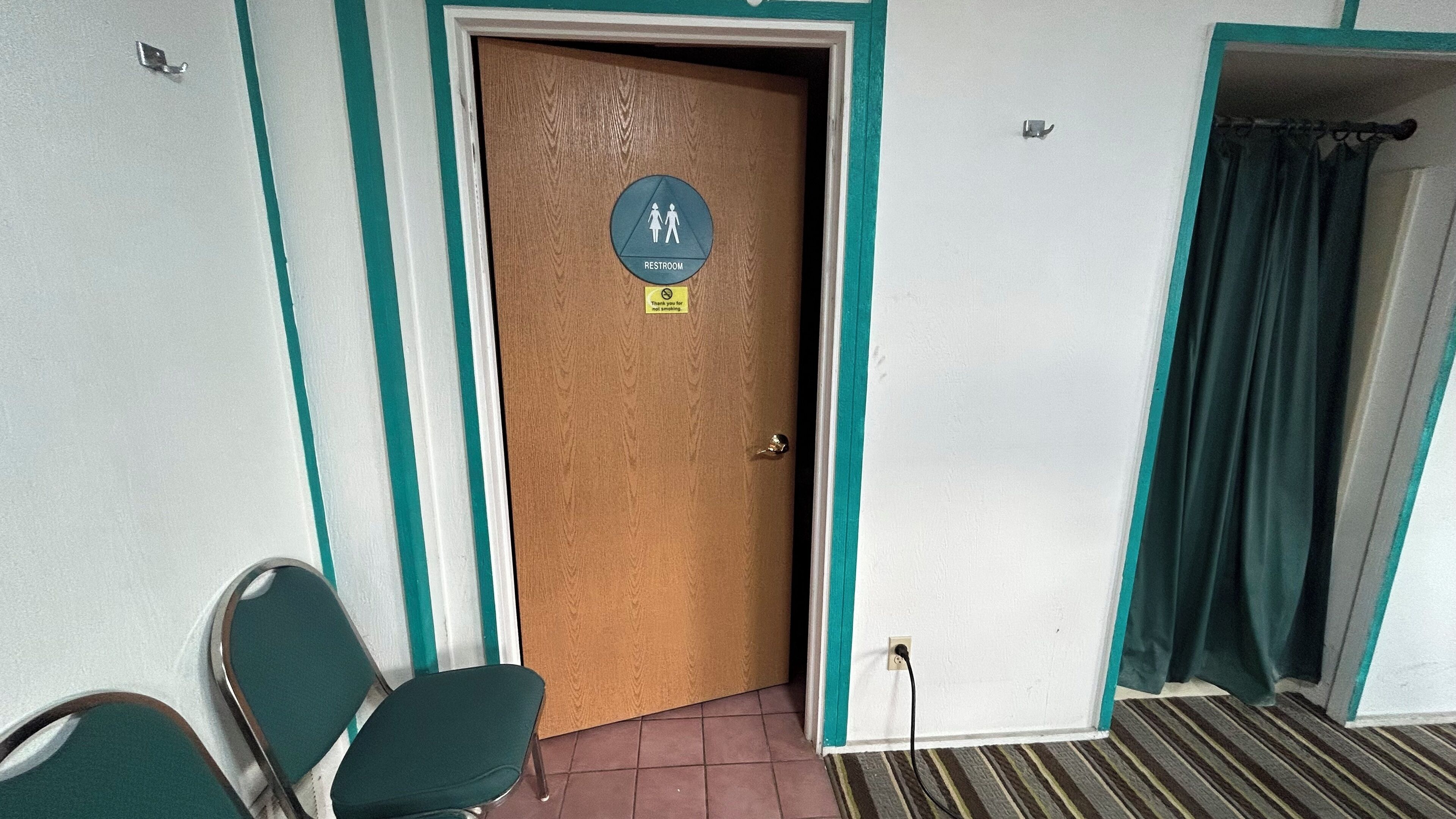 A wooden door with a restroom sign, a green chair, and a striped carpet.
