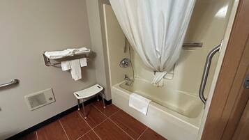 Een badkamer met een bad, een douchegordijn, een handdoekrek met handdoeken, een klein krukje en een handgreep.