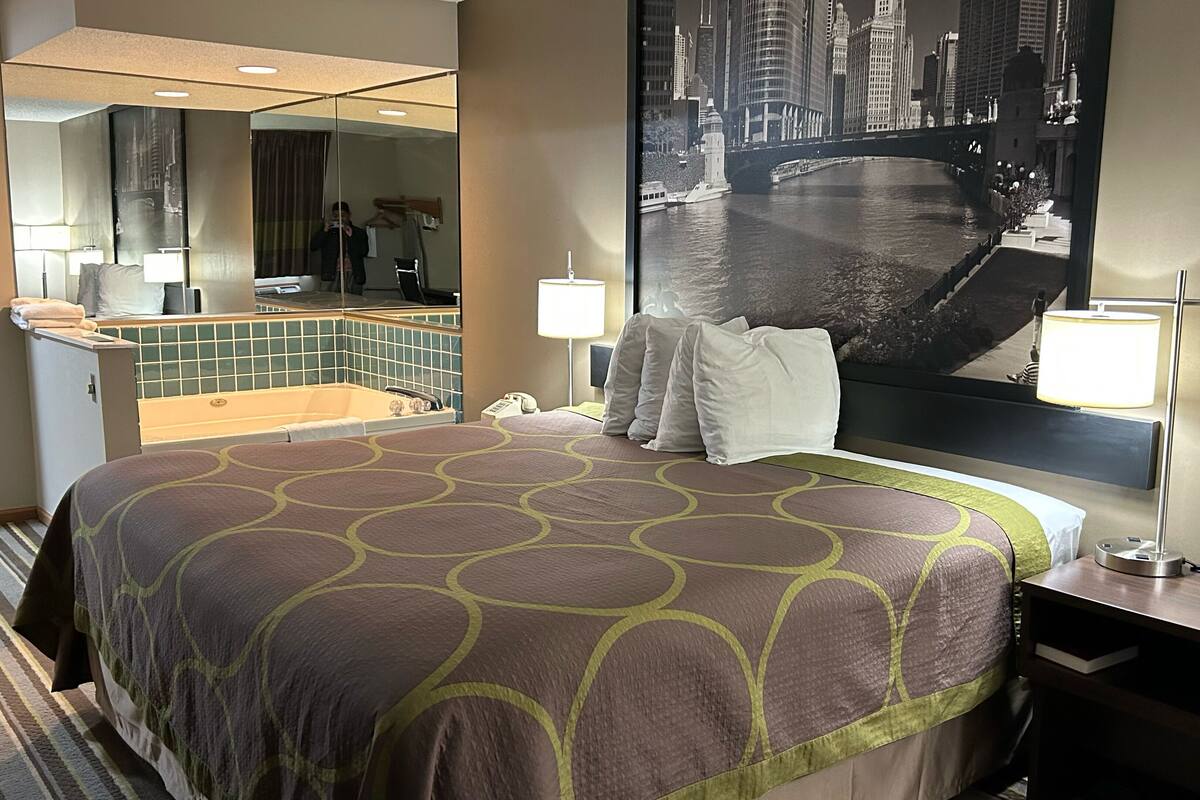 Habitación de hotel con una cama grande, baño con bañera, espejo amplio y vista a la ciudad.