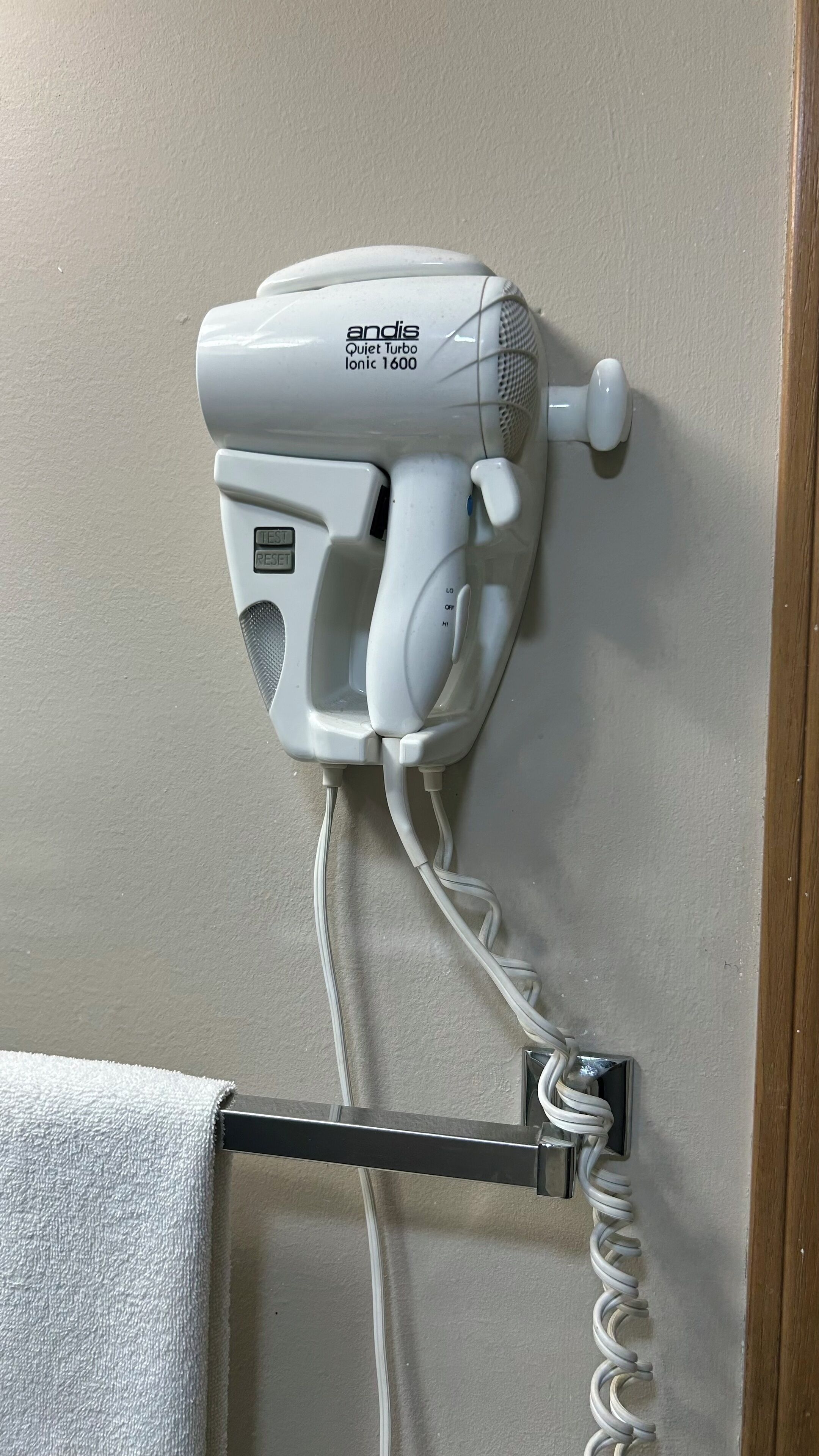 A white hair dryer mounted on a wall with a power cord.