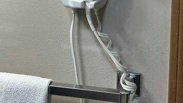 A white hair dryer mounted on a wall with a power cord.