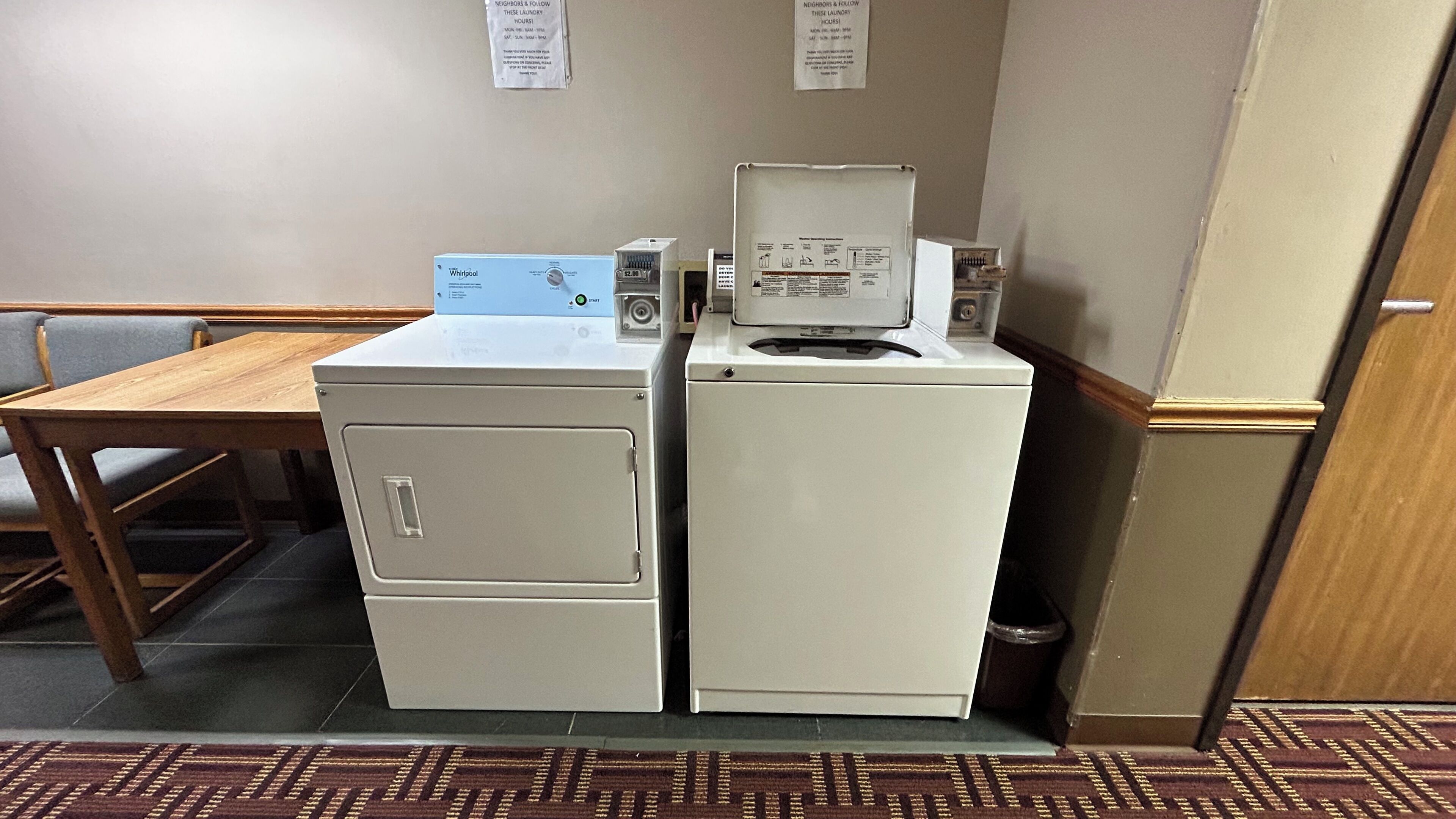 A compact laundry area with a Whirlpool washer and dryer, a wooden table, and a patterned rug.
