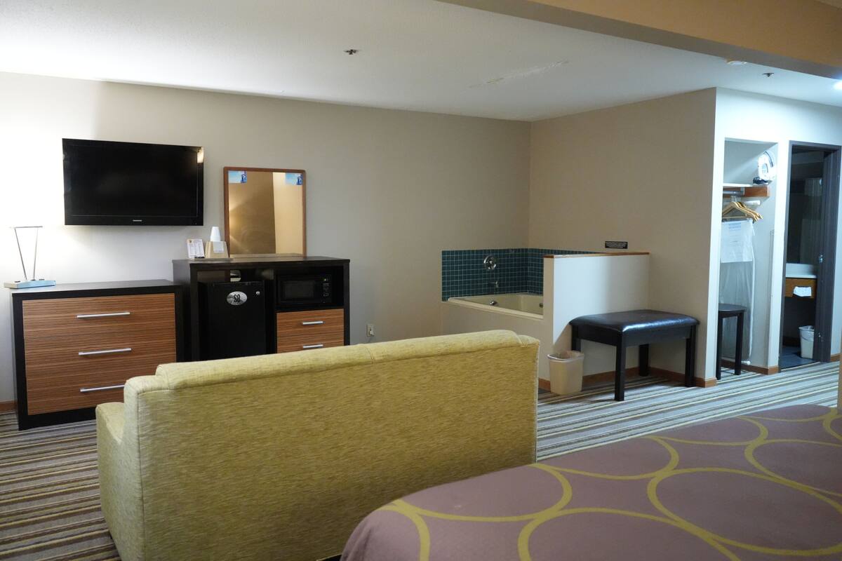Habitación de hotel con cama, escritorio con televisor de pantalla plana, minibar, baño con bañera y perchero.
