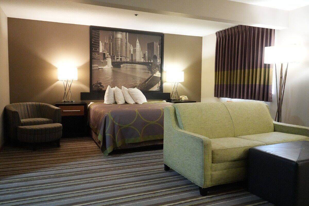 Habitación de hotel con cama, dos sillones, una mesita de noche, una lámpara y un cuadro grande con una vista panorámica de la ciudad.