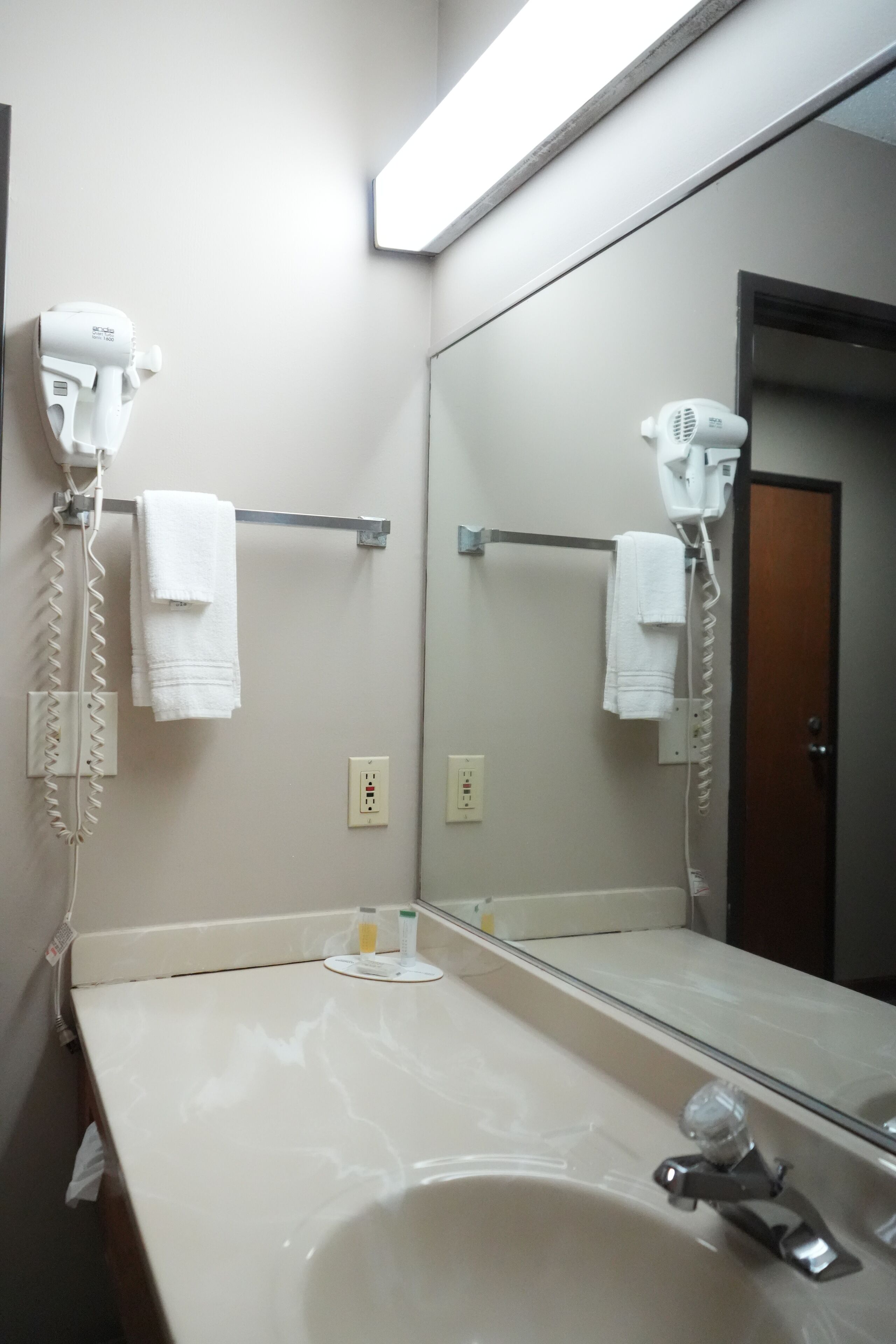 A bathroom with a sink, a mirror, and two hair dryers mounted on the wall.