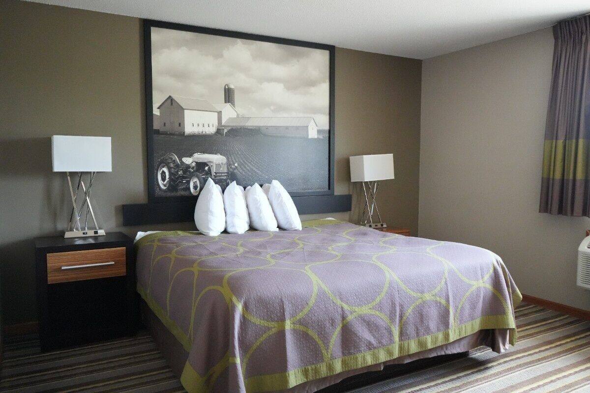 Una habitación de hotel con una cama grande, dos mesitas de noche con lámparas, un cuadro grande en la pared y una alfombra a rayas.