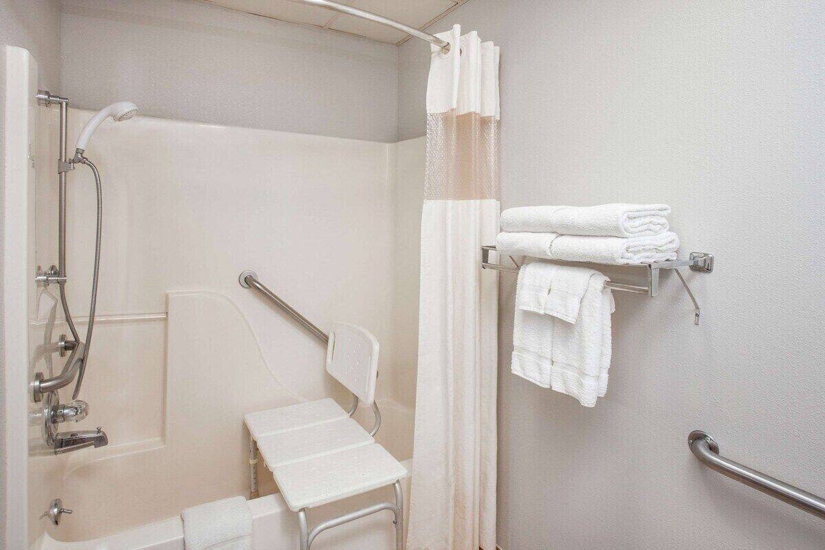 Un baño con ducha, inodoro con barra de apoyo y perchero con toallas dobladas.
