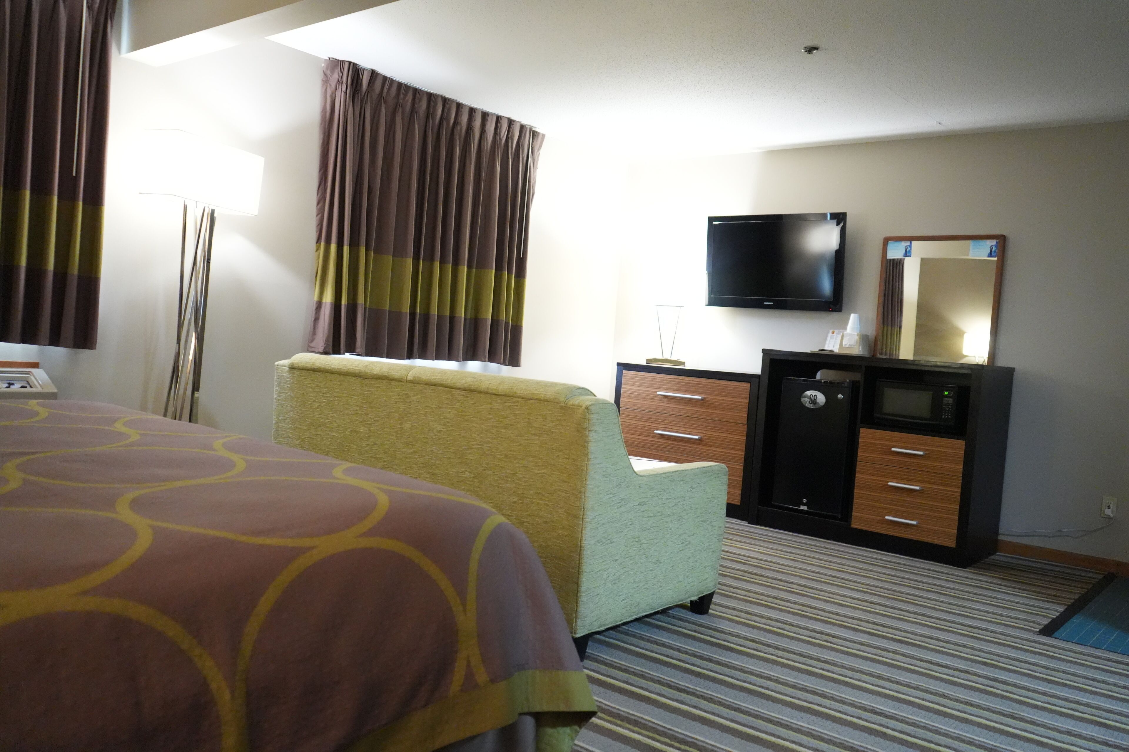 A hotel room with a bed, a desk, a television, a safe, and a mirror.