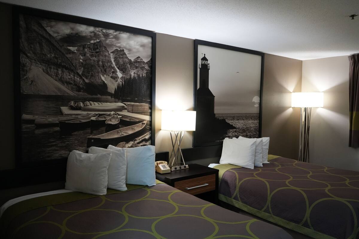 Habitación de hotel con dos camas, un cuadro grande enmarcados de un paisaje montañoso, una mesita de noche con una lámpara y un espejo en la pared.